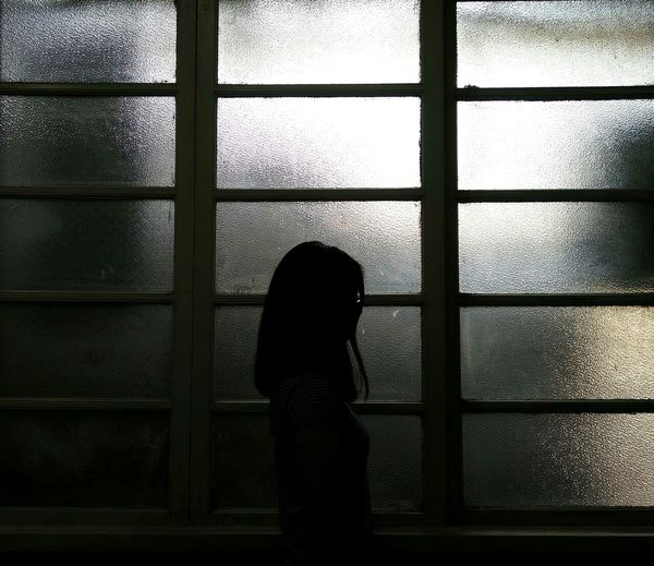 Silhouette of girl standing by window