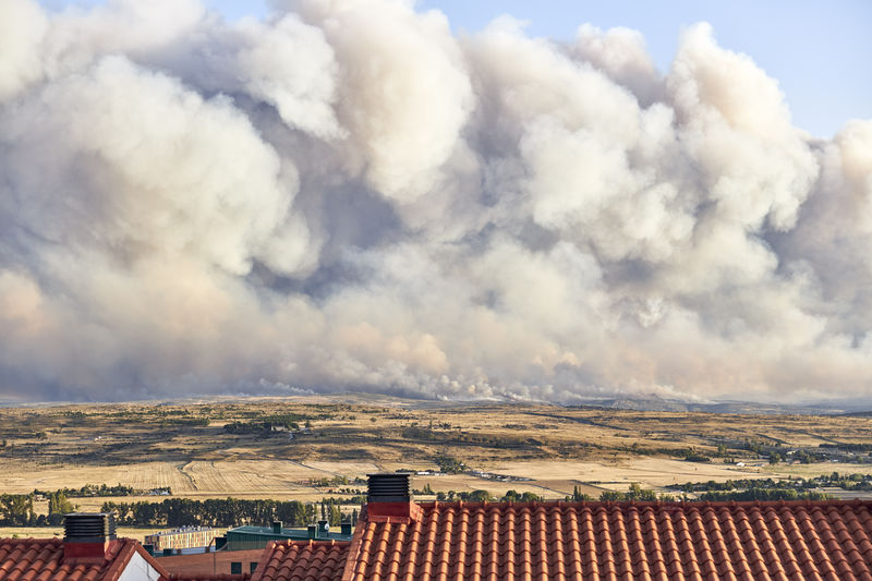 Photograph of a large forest fire with a large column of smoke on a hillside near a city