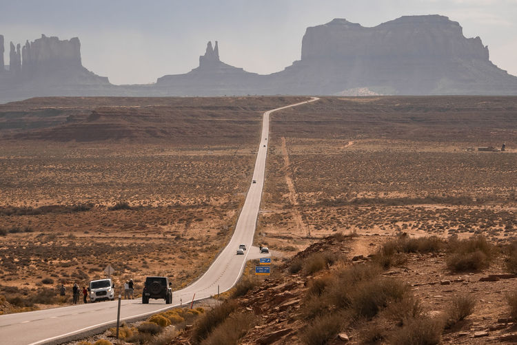 Cars on road amidst landscape leading towards monument valley during summer