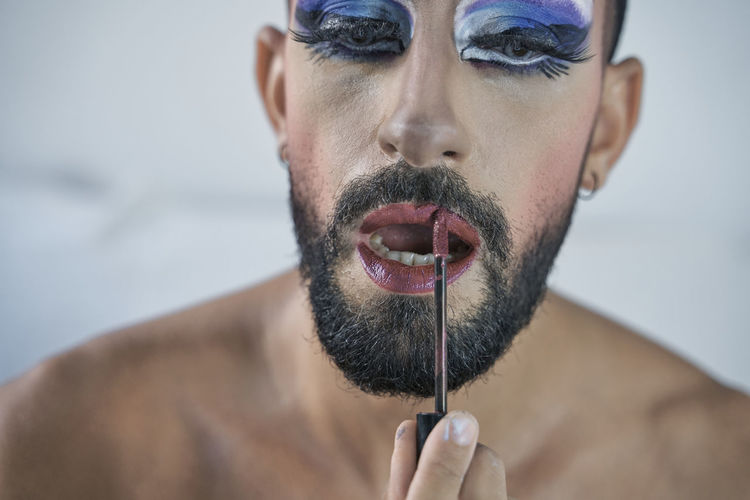 Man with blue eye make-up applying lipstick at home