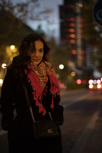 Portrait of smiling woman standing in city at dusk