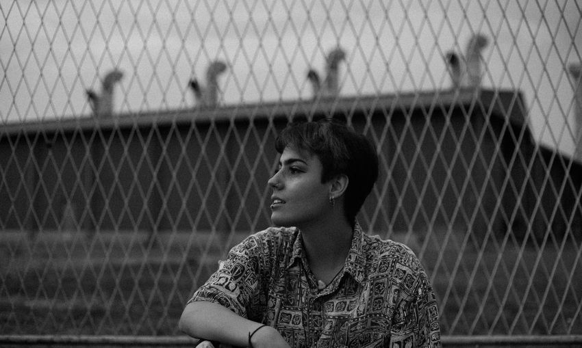 Portrait of young man looking through chainlink fence