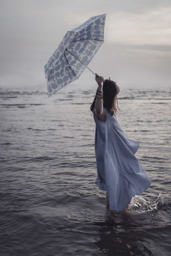 Side view of woman holding umbrella while standing in sea against sky