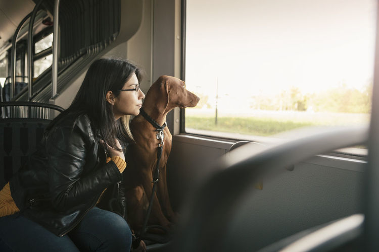 Young woman and dog looking through window while sitting in cable car