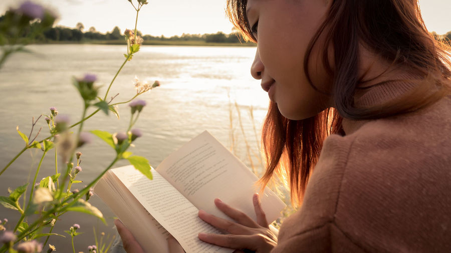Midsection of woman reading book against plants