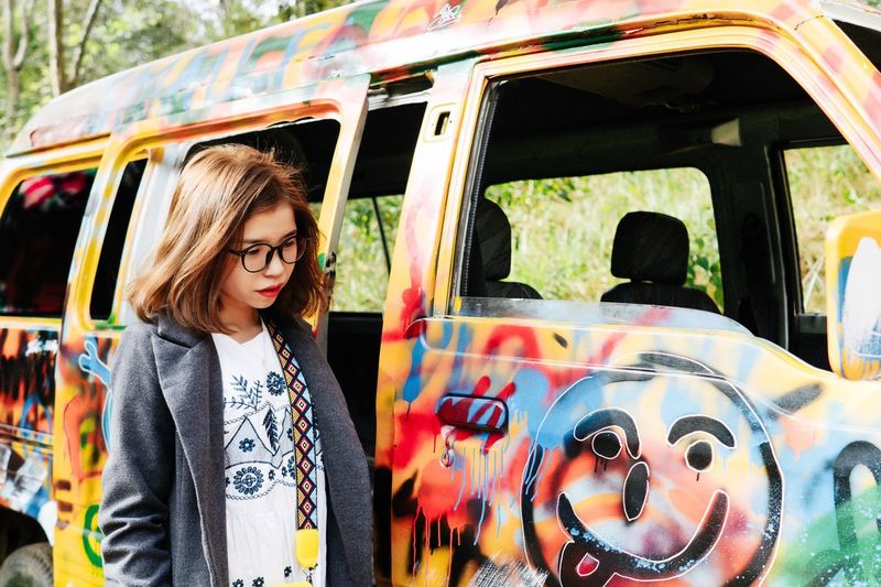 Thoughtful young woman standing by colorful painted van