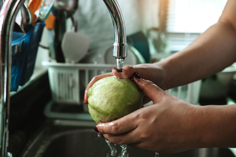 Cropped hand of woman cleaning fruit at sink