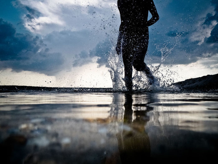 Low section of man splashing water in sea against sky