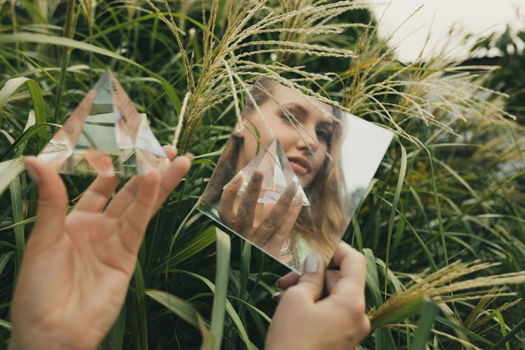 Reflection of woman holding prism in mirror against plants