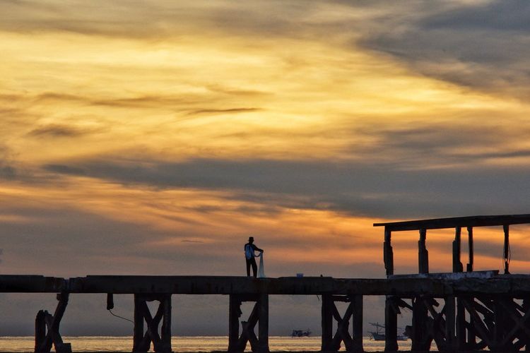 Silhouette people standing on pier by sea against sky during sunset