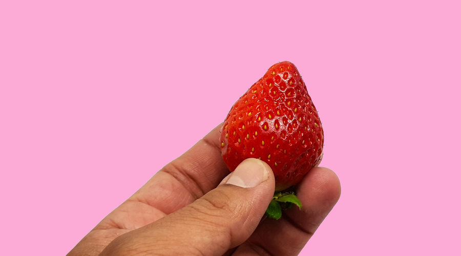 Cropped image of hand holding strawberry against white background