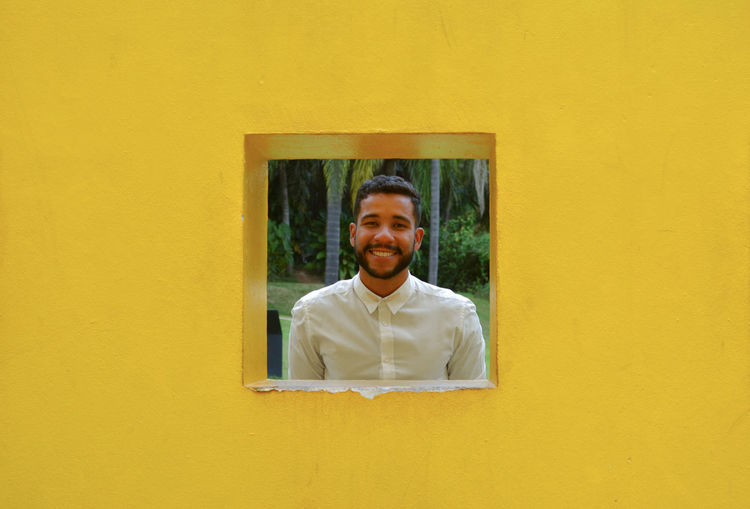 Portrait of smiling young man seen through window on yellow wall