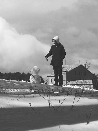 Woman standing by snowman on field against cloudy sky