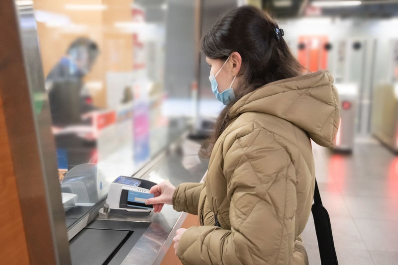Young woman in a mask buys a subway ticket and pays with credit card contactless