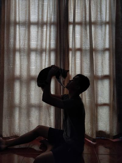 Side view of man playing with cat at home