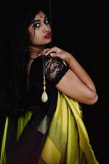 Portrait of young woman wearing sari standing against black background