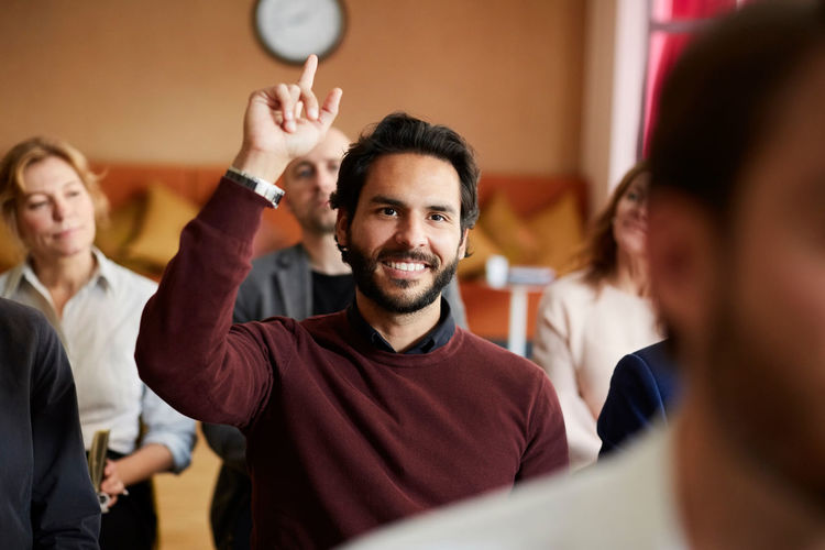 Smiling businessman with hand raised sitting in office seminar