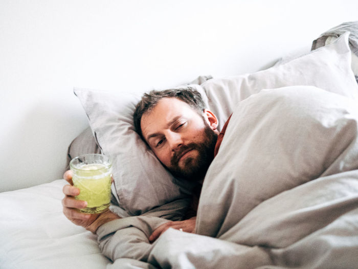 Portrait of sick man holding drink while lying on bed at home