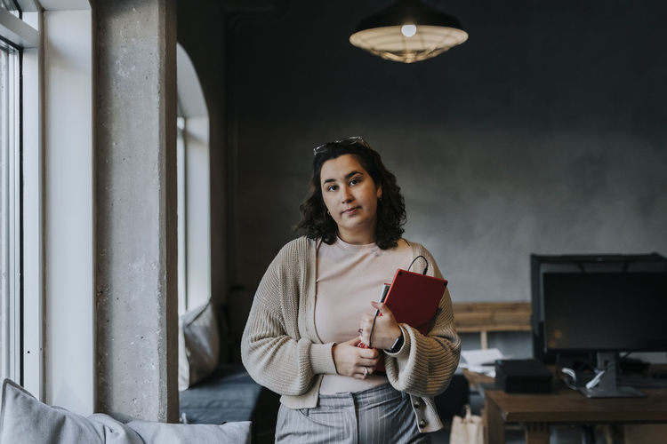 Portrait of young woman standing against wall