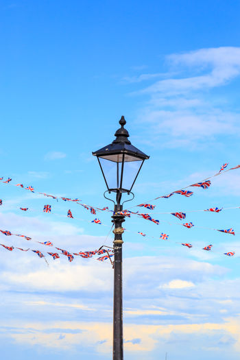 Low angle view of lighting equipment amidst british flags against blue sky