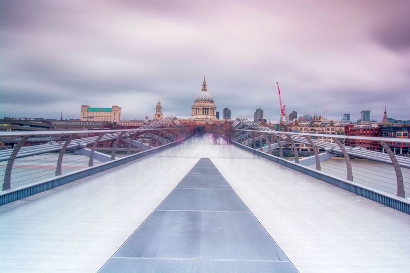 Digital composite image of bridge and buildings against cloudy sky