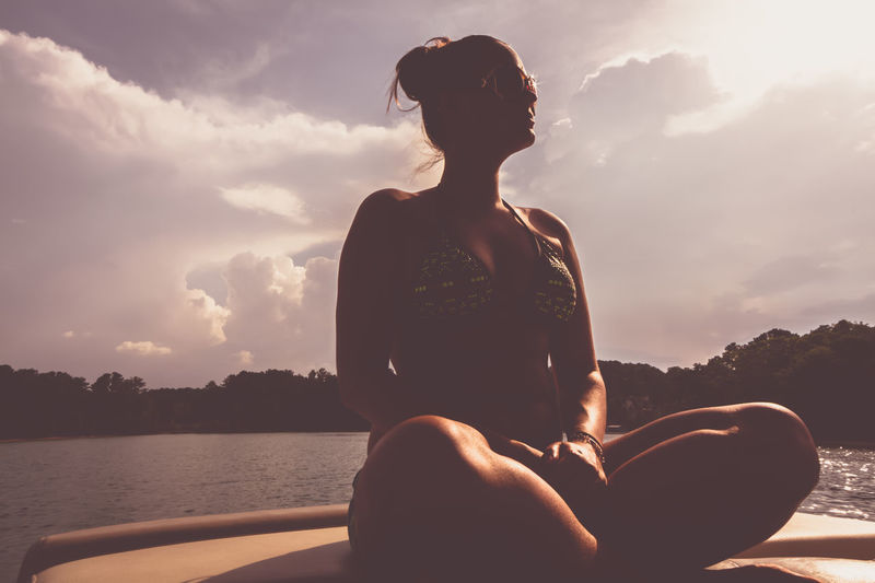 Woman sitting on boat in sea against sky during sunset