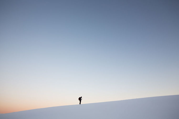 Man standing on snowcapped mountain against clear sky at sunset