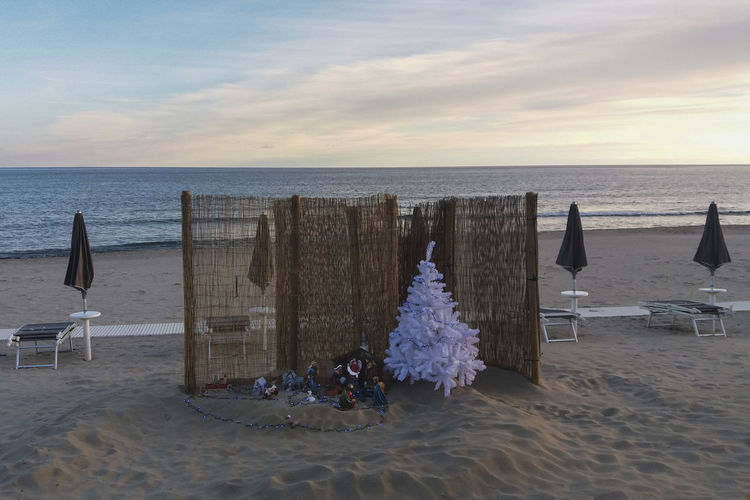 Deck chairs on beach against sky during sunset