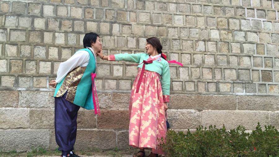 Full length of loving couple wearing hanbok standing by wall
