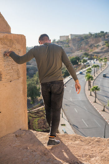 Side view of man standing on retaining wall against sky