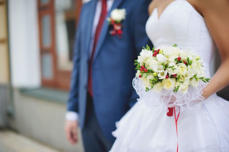 Midsection of bride with groom holding flower bouquet
