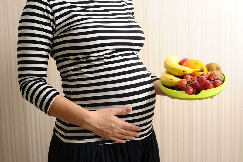 Midsection of pregnant woman holding a fruit plate