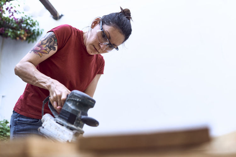 Young woman polishing a wooden plank with a power sander