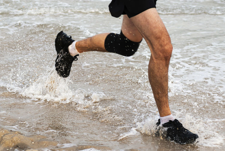 Low section of man running at sea shore