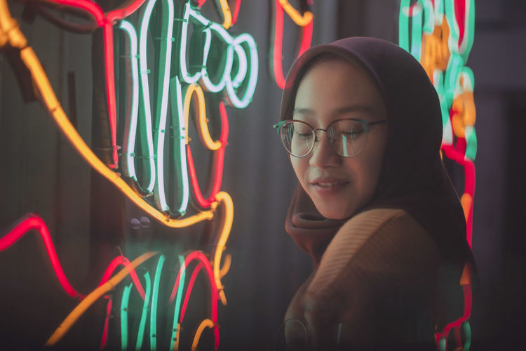 Smiling woman against multi colored lights on wall