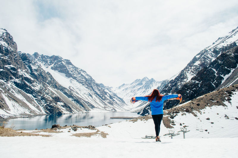 Full length of woman standing by lake against snowcapped mountain