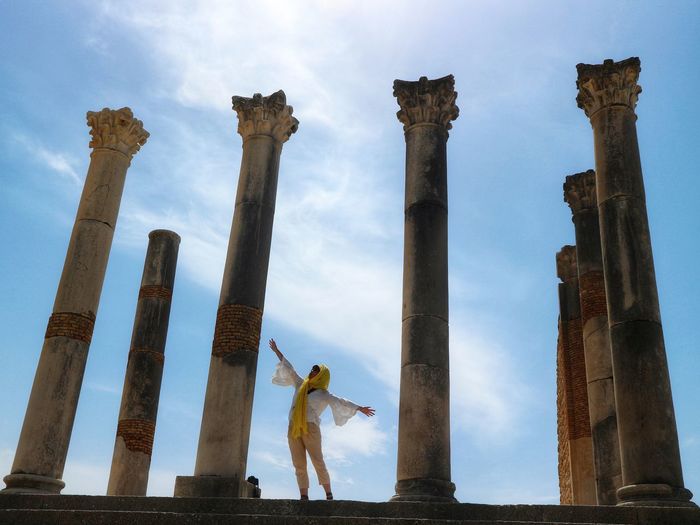 Woman with arms outstretched standing amidst columns of old ruins