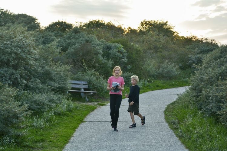 Two children running on footpath, in the north sea dunes 
by road against sky