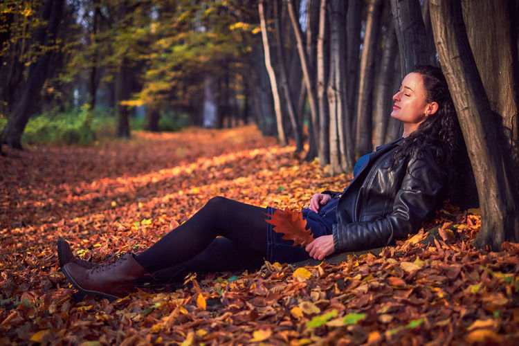 Young woman sitting on leaves at forest during autumn