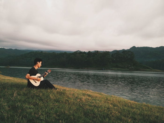 Man playing guitar at lakeshore against sky