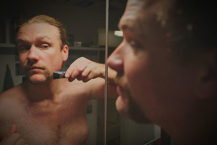 Man shaving beard looking at mirror