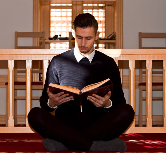 Young man reading koran against wooden railing