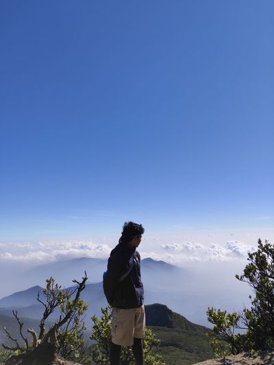 Man standing by mountain against blue sky