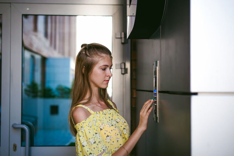 Young woman entering password on security system by door