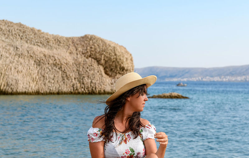 Portrait of beautiful young woman wearing summer dress and sun hat standing on beach.
