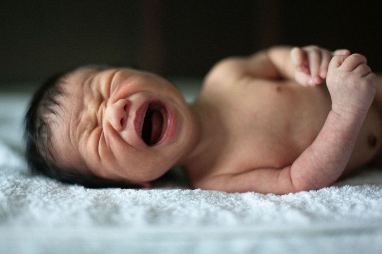 Close-up of newborn baby boy crying while lying on bed at home