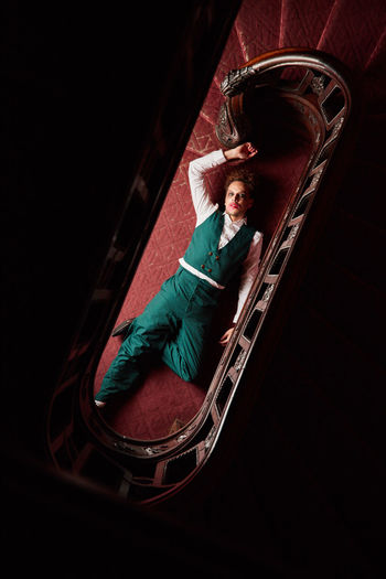 Top view of talented male actor lying on floor near staircase and pretending being dead during creative performance