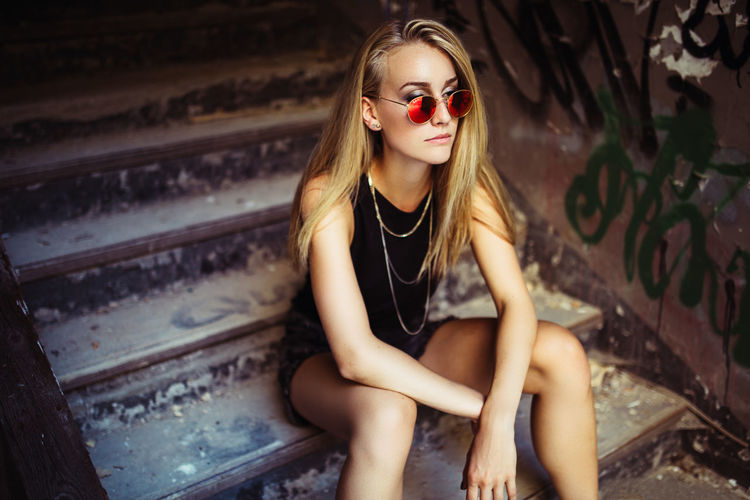 Young woman sitting on dirty stairs looking away from camera