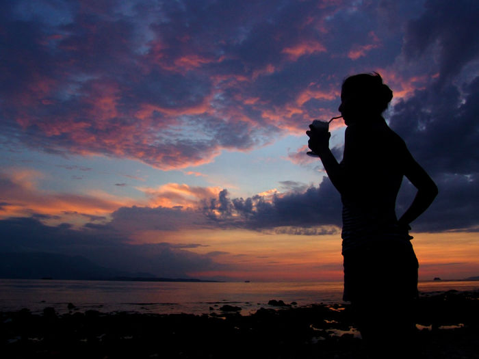 Silhouette woman photographing sea at sunset