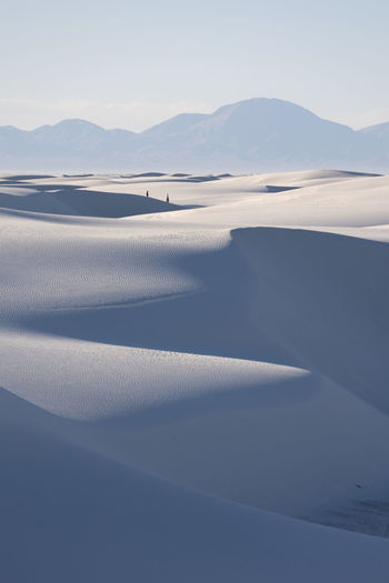 Two hikers in the distance traverse the gypsum sand dunes in white sands national park